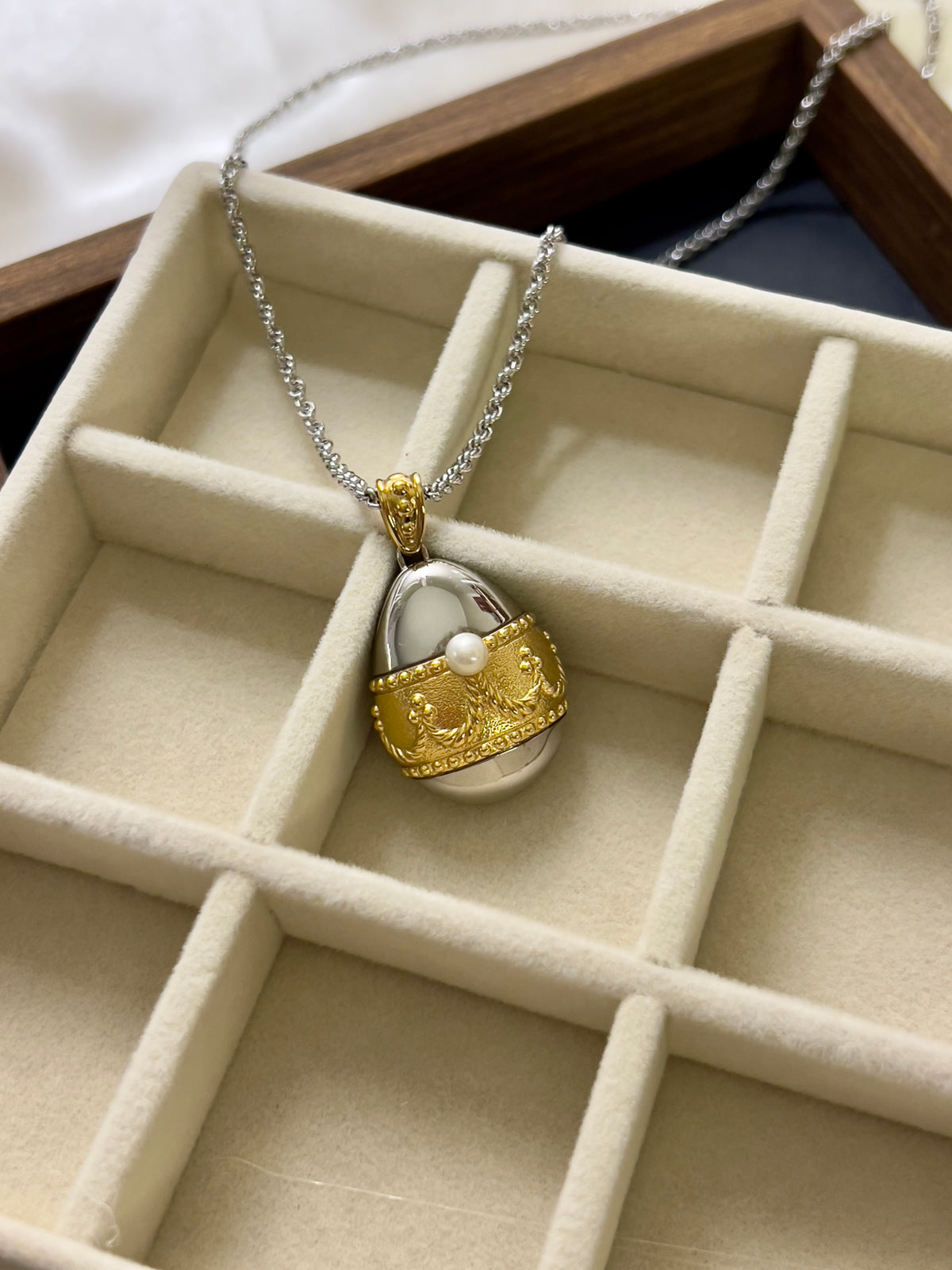 Tasaki egg pendant watch with a gold-tone case, white dial, and pearl detail.