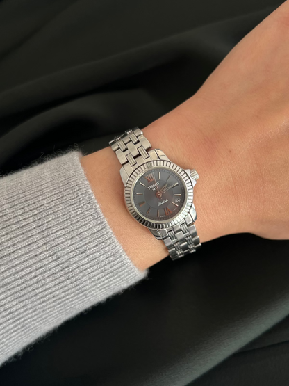 Tissot Ballade watch worn on wrist with grey dial, fluted stainless steel bezel, date window and polished steel bracelet