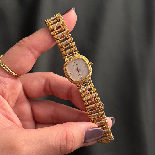 Tissot gold ladies watch with silver and gold striped dial shown on a wrist.
