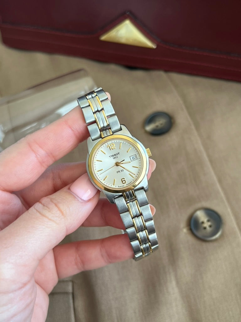 Handheld Tissot PR 50 showing its 28 mm round steel case, gold tone bezel and date at three
