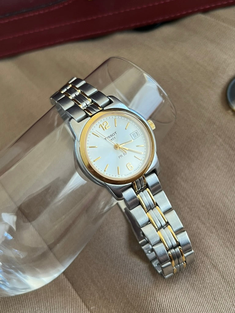 Close view of the Tissot PR 50 pale silver dial, gold tone 12 and 6 numerals, date window and smooth gold tone bezel