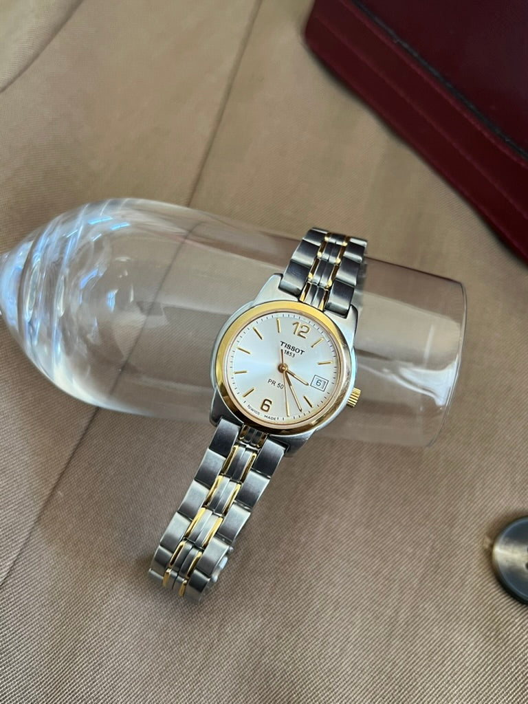 Tissot PR 50 round case and two tone steel bracelet with twin gold tone accents, resting on a clear display
