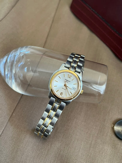 Tissot PR 50 round case and two tone steel bracelet with twin gold tone accents, resting on a clear display