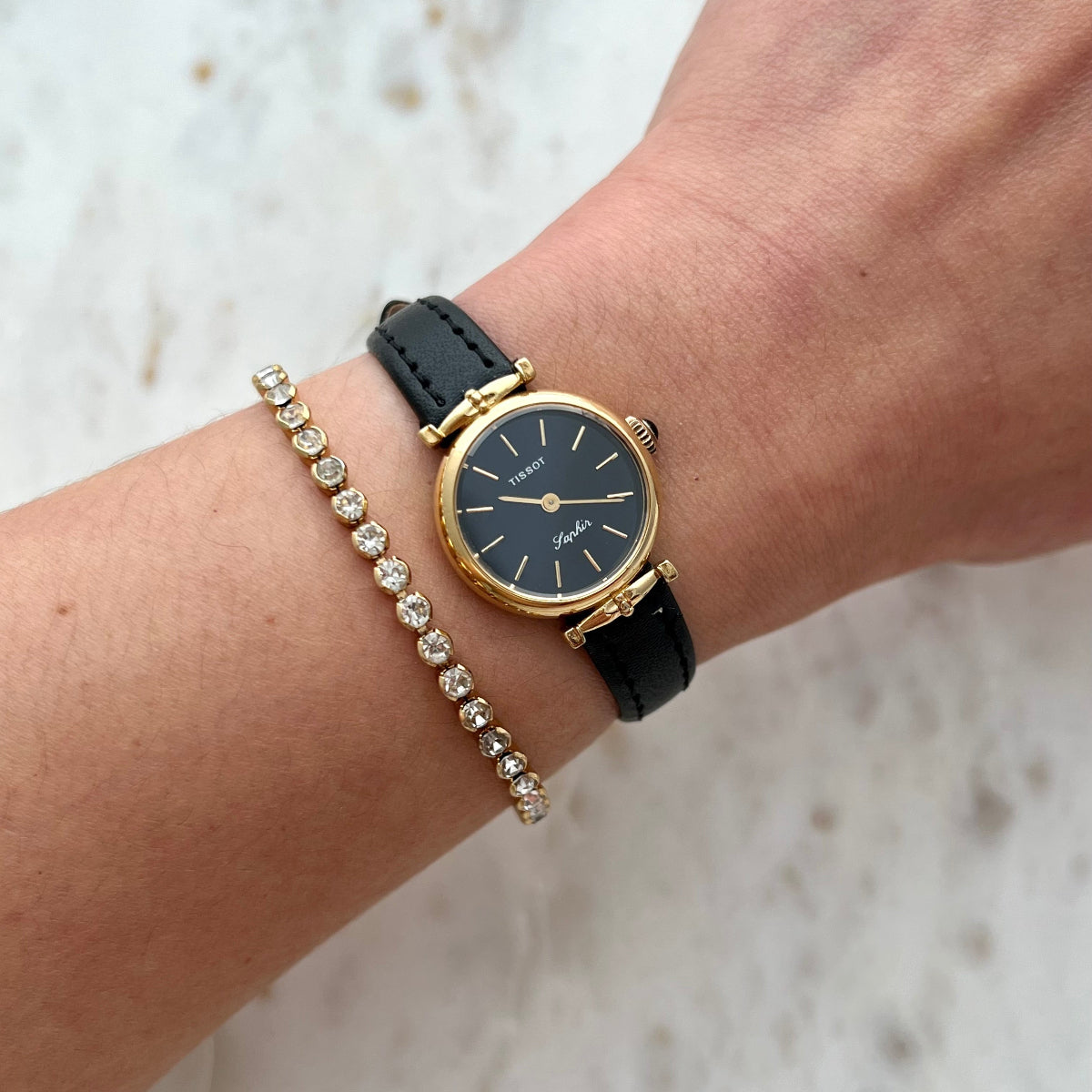 Tissot Saphir women’s watch with black dial, gold tone case and black leather strap worn on wrist