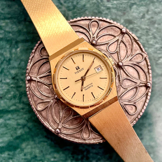 Tissot Seastar gold-tone watch with textured bracelet on a green surface.