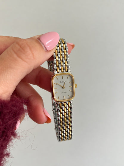 Tissot Stylist rectangular watch and silver and gold tone bracelet held upright.