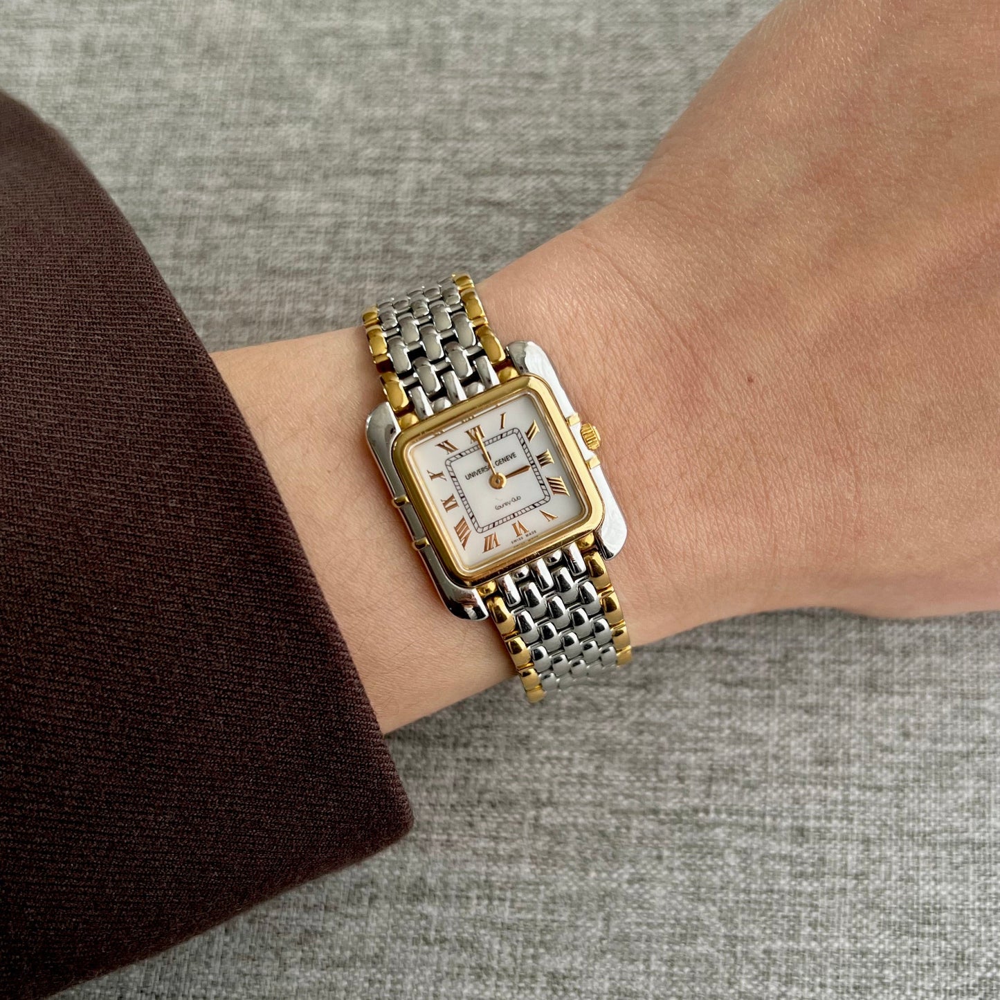 Universal Genève square luxury women’s watch with white Roman numeral dial and two tone gold and silver bracelet worn on wrist