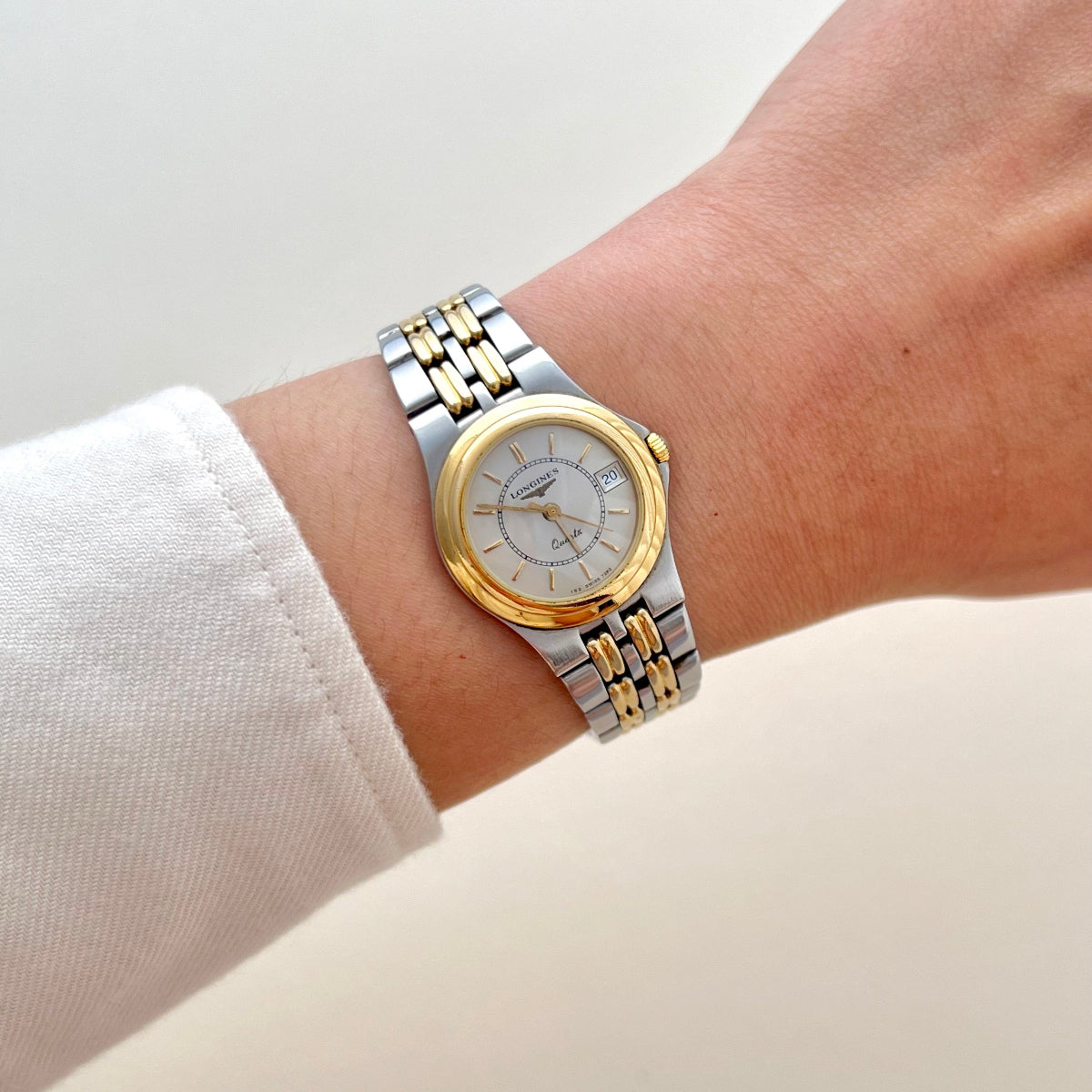 Vintage Longines women’s two-tone quartz watch with a white dial, gold-tone bezel, date display and integrated bracelet worn on wrist