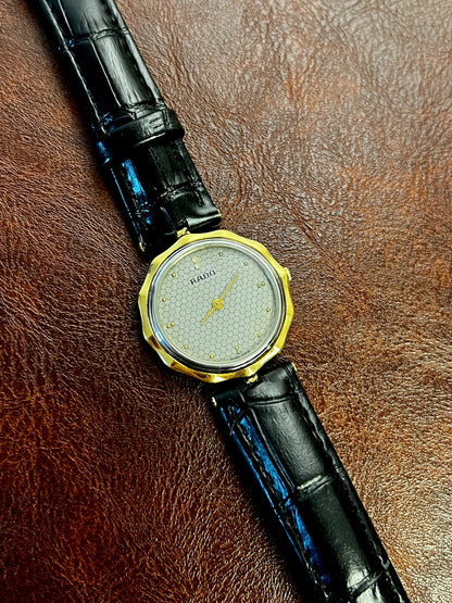 Vintage Rado women's watch with a flower-shaped two-tone case and honeycomb dial, shown full length with the black leather strap.