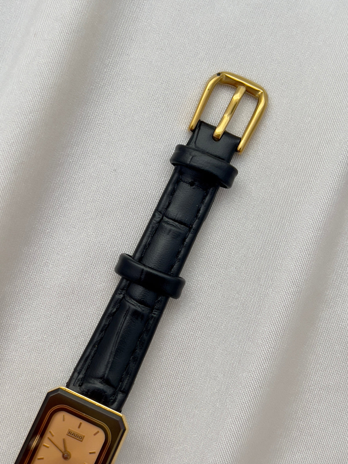 Vintage Rado DiaStar tank women's watch with a champagne dial and black leather strap, shown with its gold-tone buckle.