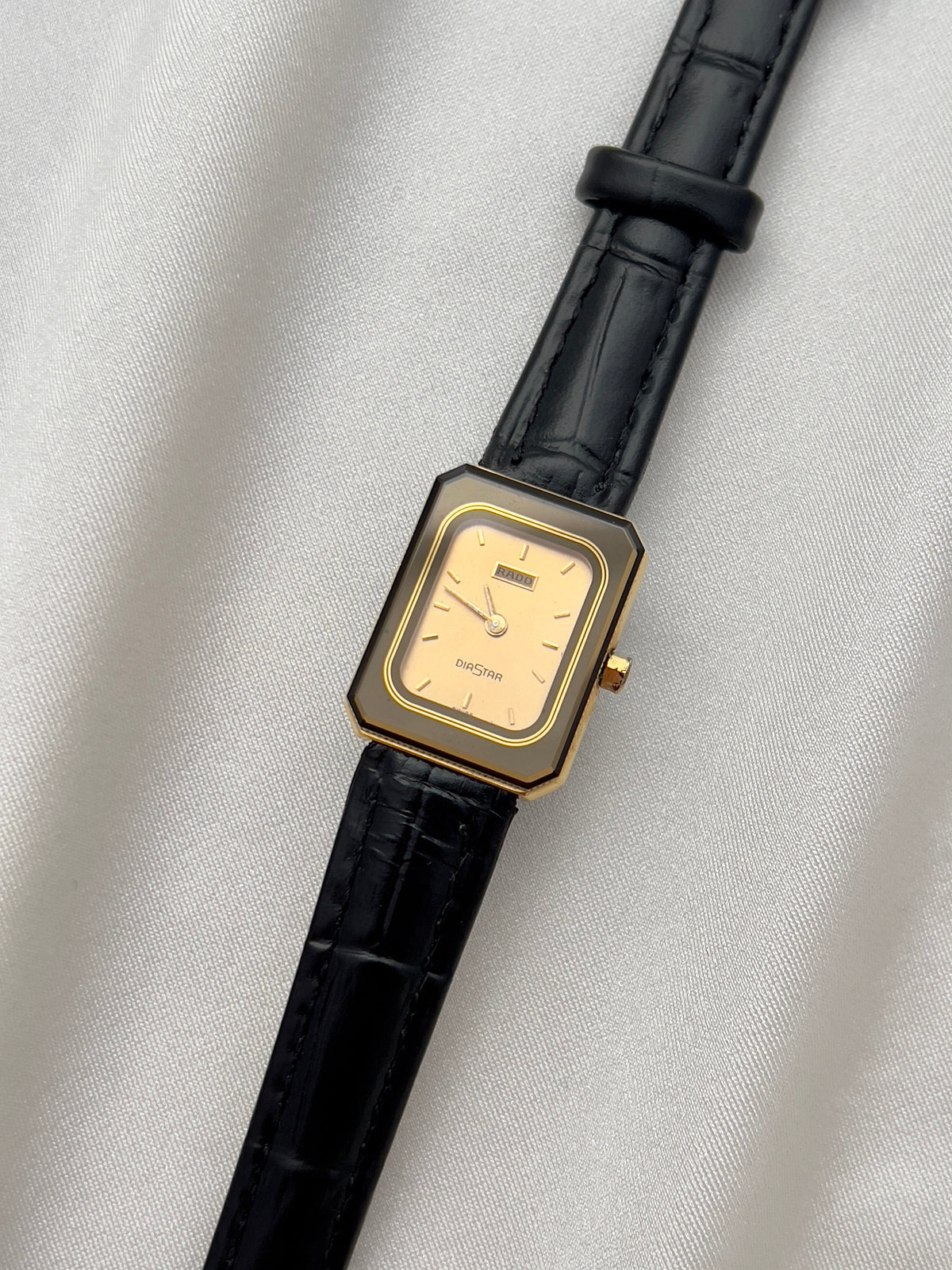 Vintage Rado DiaStar tank women's watch with a champagne dial and black leather strap, shown straight on against white fabric.