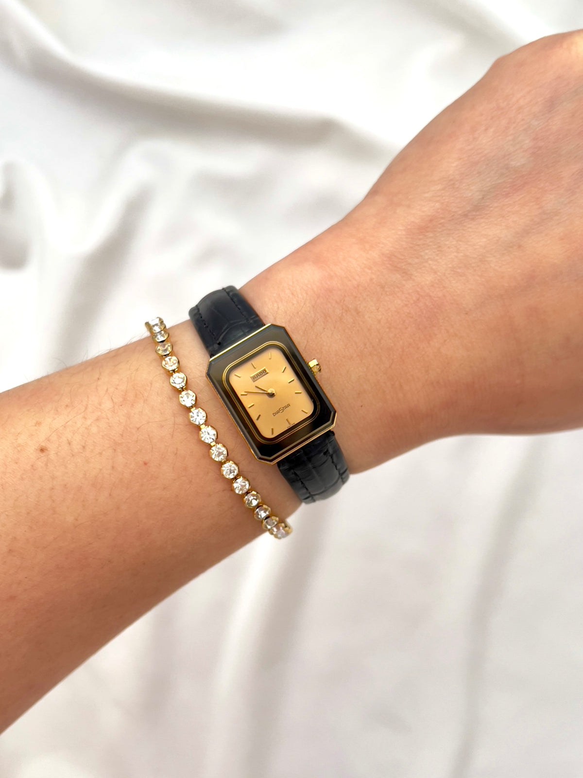 Vintage Rado DiaStar tank women's watch with a champagne dial and black leather strap, worn on the wrist.