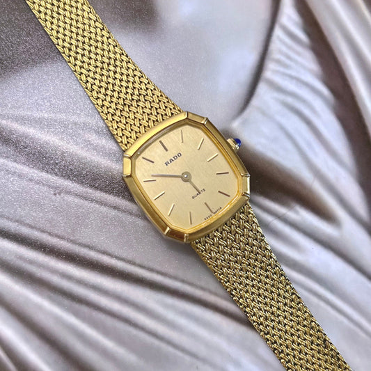 Vintage Rado gold mesh women's watch with a champagne dial and faceted case, shown in a close front view on a classical sculpture.