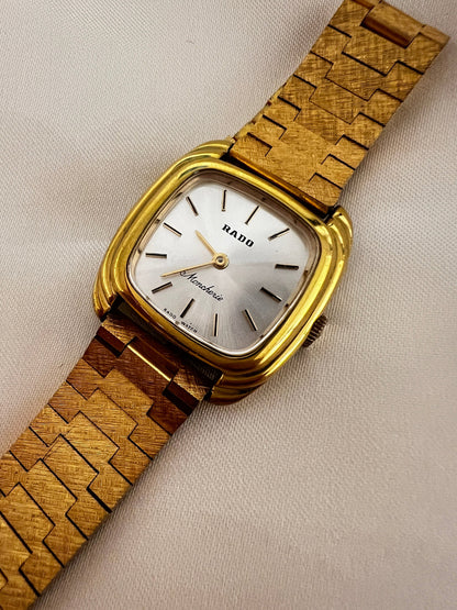 Vintage Rado Moncherie women's watch with a silver dial, double gold-tone frame and bracelet, shown at an angle to reveal the double-frame case.