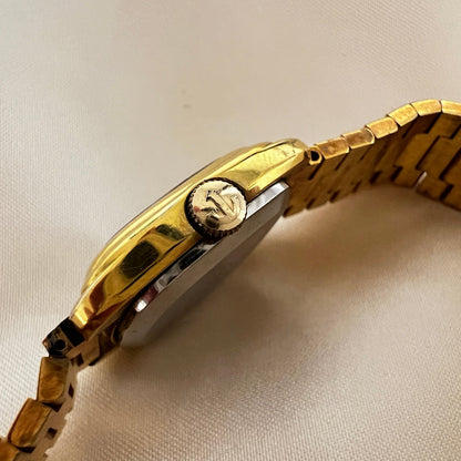 Vintage Rado Moncherie women's watch with a silver dial, double gold-tone frame and bracelet, shown from the side with the signed crown.