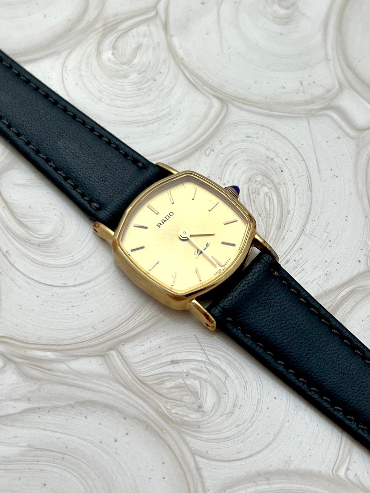Vintage Rado Soft Octo Silhouette women's watch with a gold-tone case and black leather strap, shown at an angle on white textured fabric.