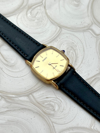 Vintage Rado Soft Octo Silhouette women's watch with a gold-tone case and black leather strap, shown at an angle on white textured fabric.