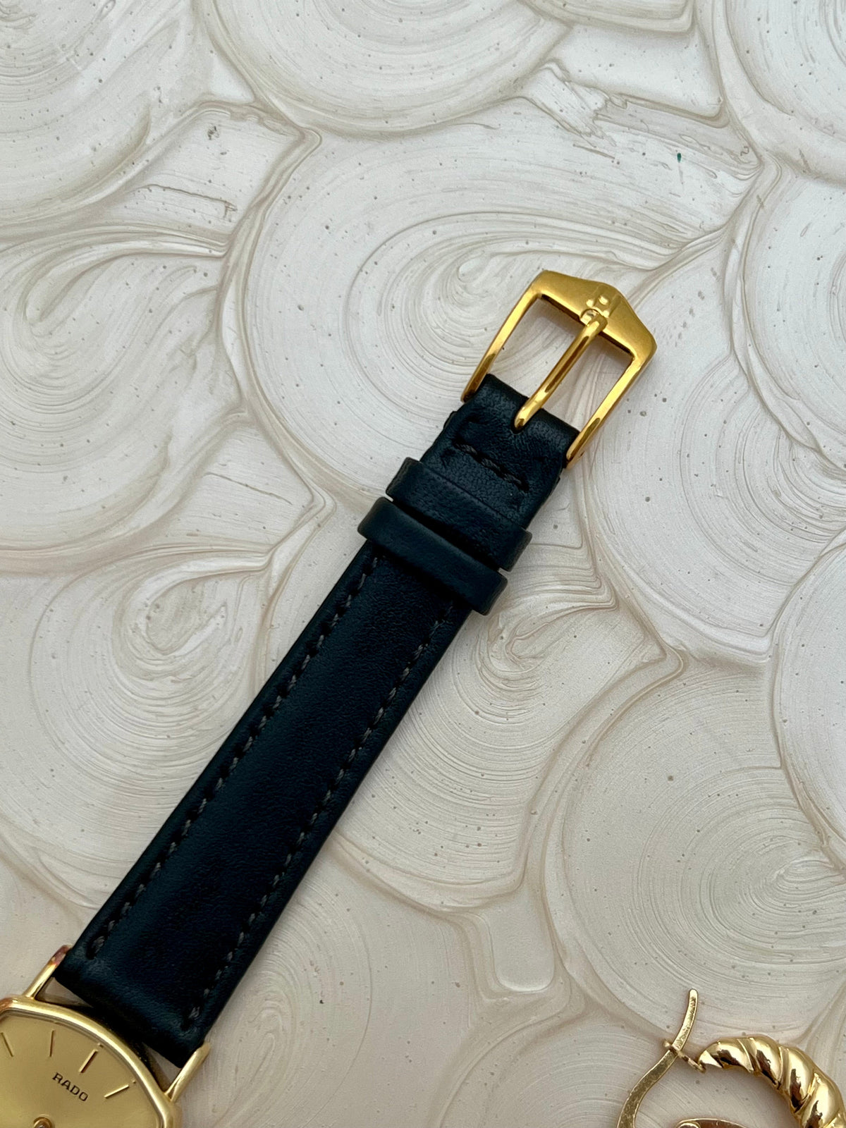 Vintage Rado Soft Octo Silhouette women's watch with a gold-tone case and black leather strap, shown with its gold-tone buckle.