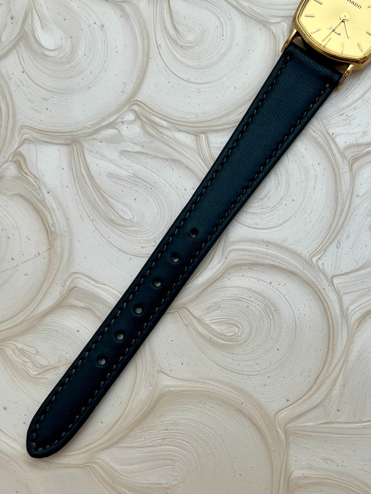 Vintage Rado Soft Octo Silhouette women's watch with a gold-tone case and black leather strap, shown with the black leather strap tip.