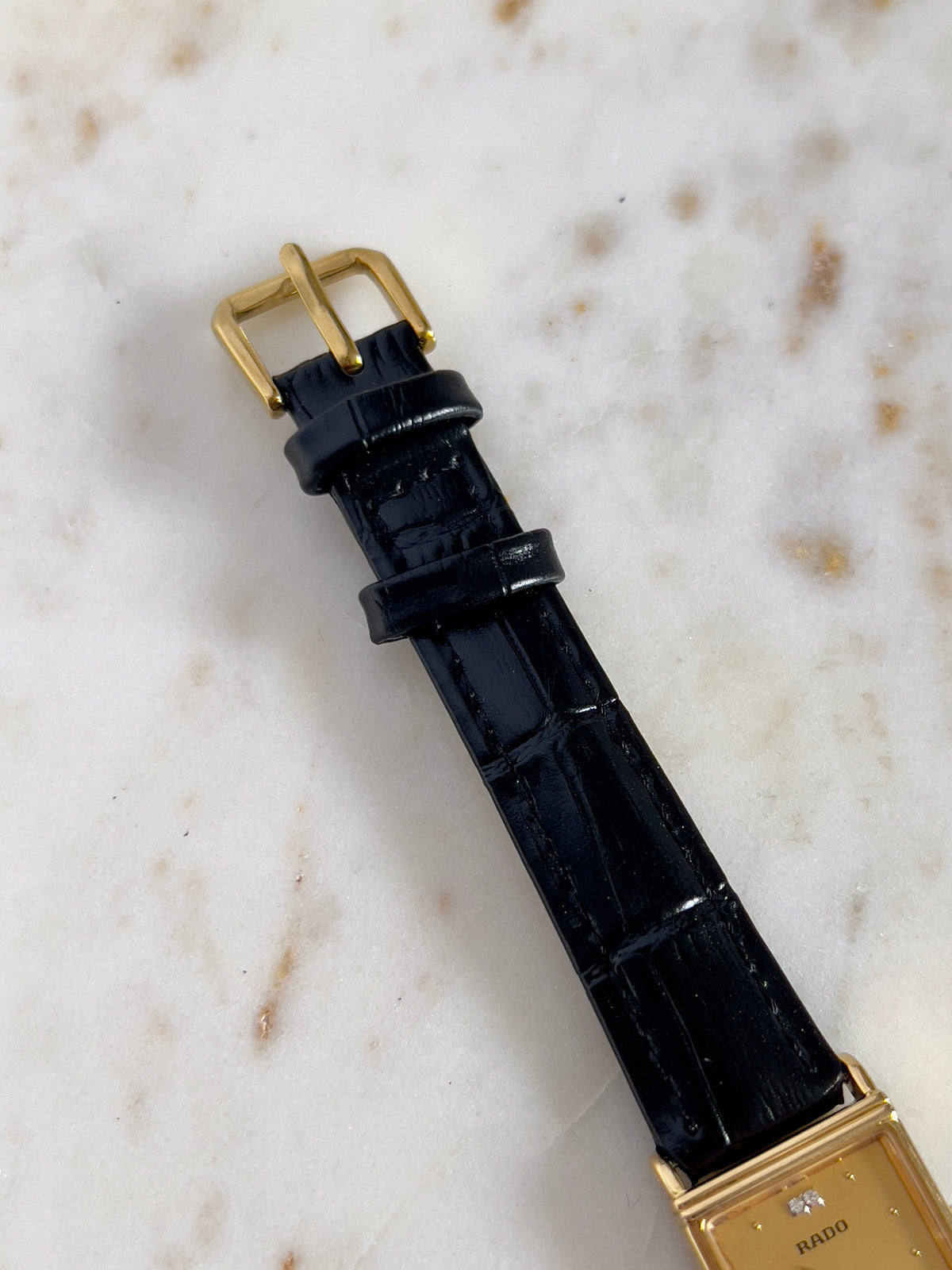 Vintage Rado tank women's watch with a gold dial, diamond accents and black leather strap, shown with its gold-tone buckle.