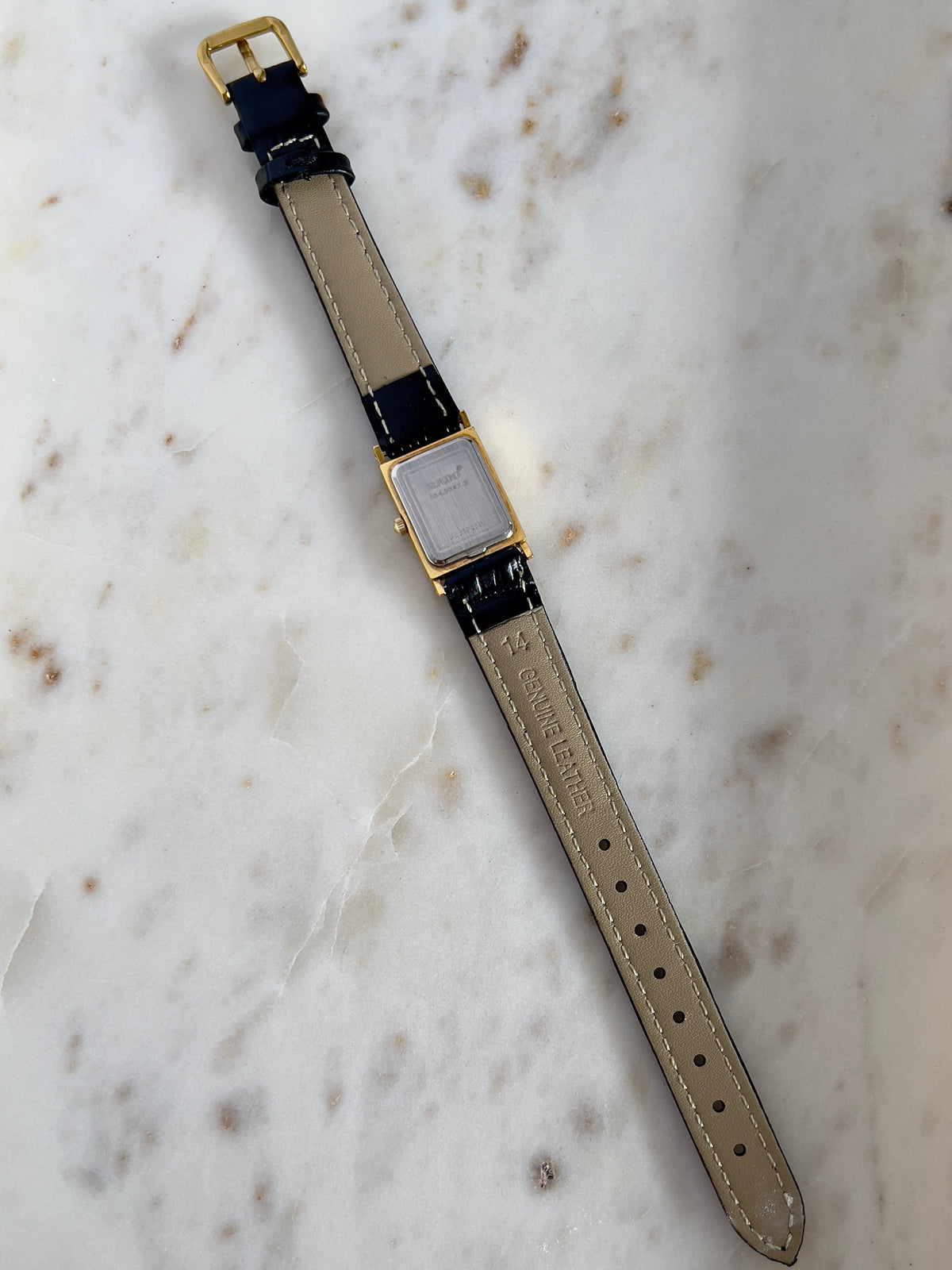 Vintage Rado tank women's watch with a gold dial, diamond accents and black leather strap, shown from the back with the full strap.