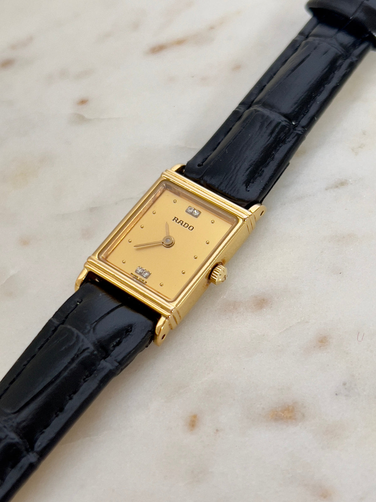 Vintage Rado tank women's watch with a gold dial, diamond accents and black leather strap, shown close to reveal the diamond dial accents.
