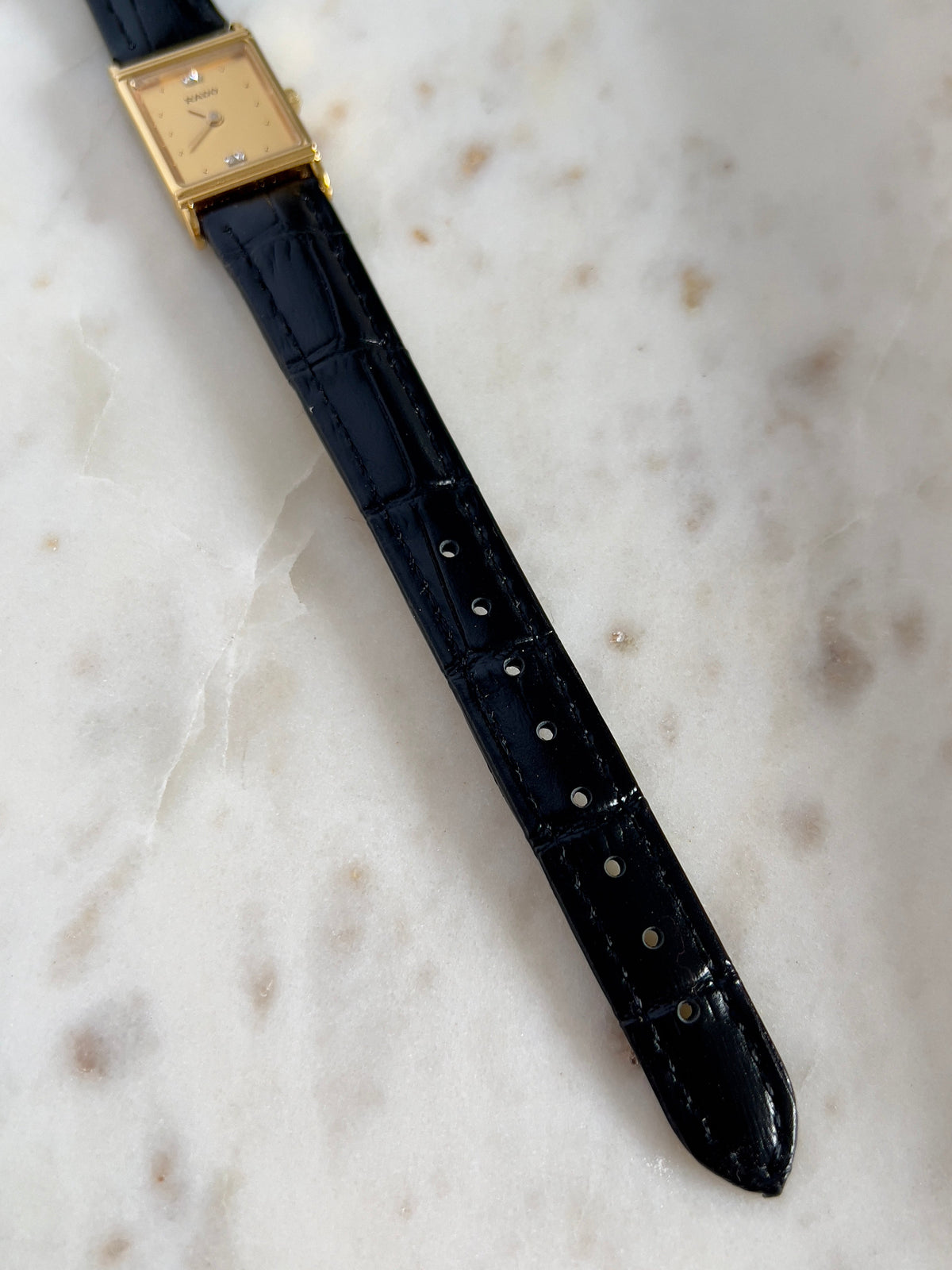 Vintage Rado tank women's watch with a gold dial, diamond accents and black leather strap, shown full length on marble.