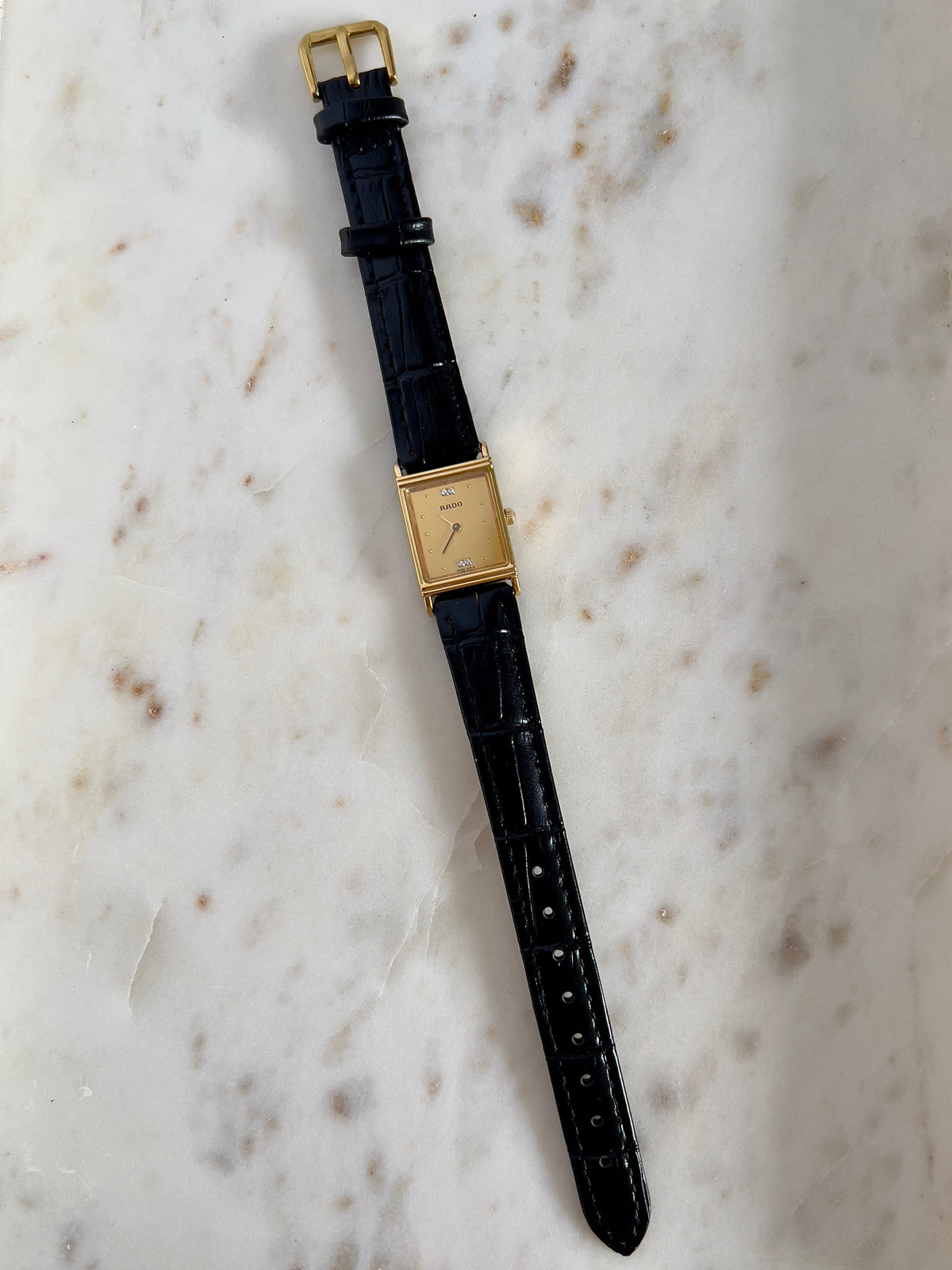 Vintage Rado tank women's watch with a gold dial, diamond accents and black leather strap, shown vertically with the leather strap.