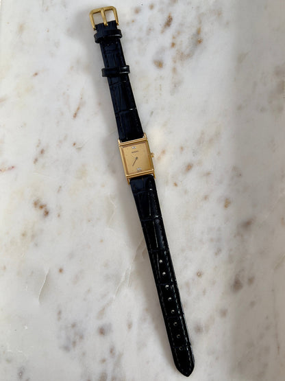 Vintage Rado tank women's watch with a gold dial, diamond accents and black leather strap, shown vertically with the leather strap.