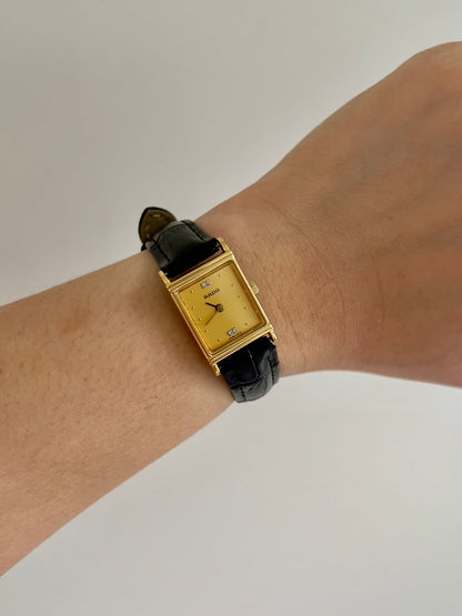Vintage Rado tank women's watch with a gold dial, diamond accents and black leather strap, worn on the wrist.