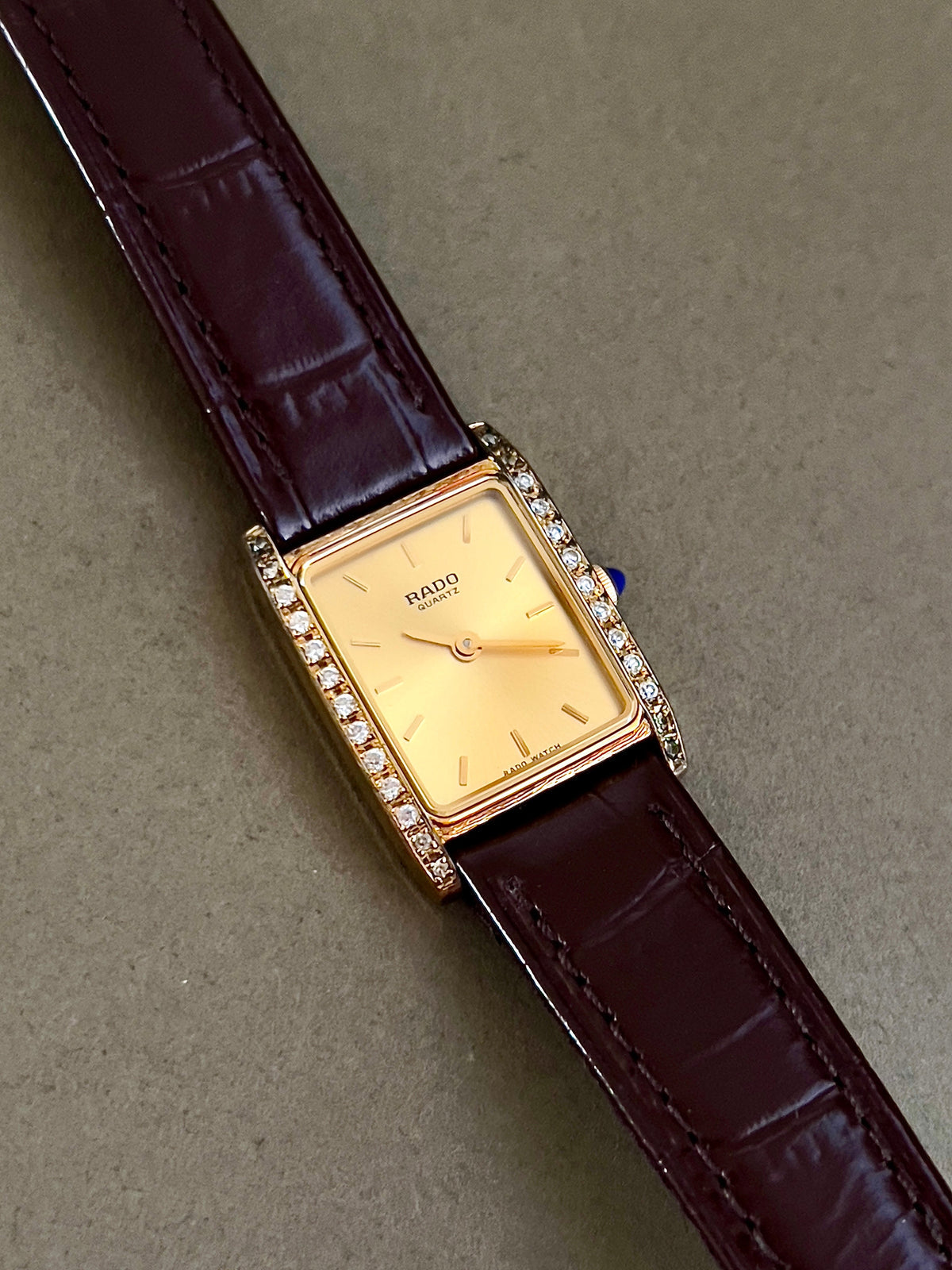 Vintage Rado tank women's watch with a champagne dial, diamond-set case and burgundy leather strap, shown at an angle with the diamond rows visible.