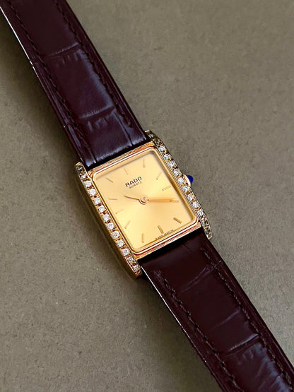 Vintage Rado tank women's watch with a champagne dial, diamond-set case and burgundy leather strap, shown at an angle with the diamond rows visible.