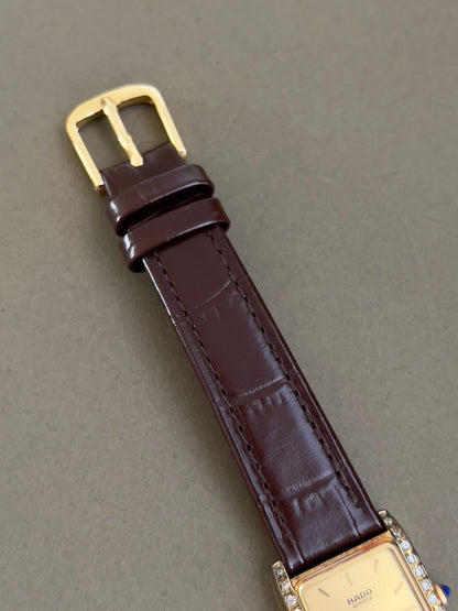 Vintage Rado tank women's watch with a champagne dial, diamond-set case and burgundy leather strap, shown with its gold-tone buckle.