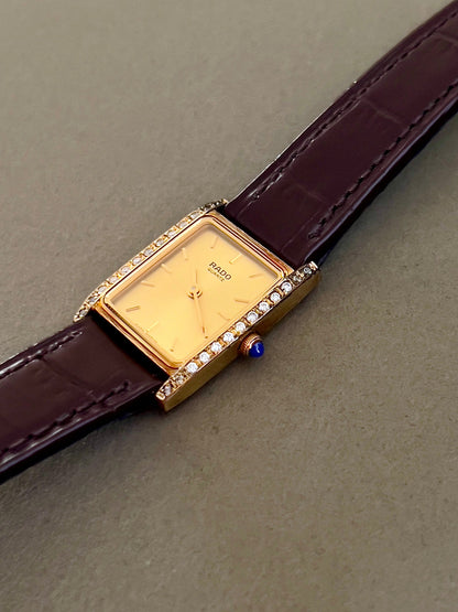 Vintage Rado tank women's watch with a champagne dial, diamond-set case and burgundy leather strap, shown in profile with the blue cabochon crown.
