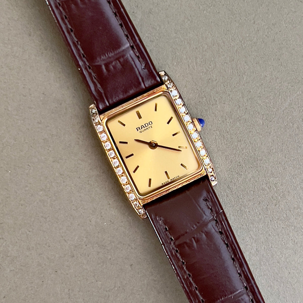 Vintage Rado tank women's watch with a champagne dial, diamond-set case and burgundy leather strap, shown in a close view of the diamond-set case.