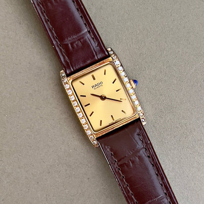 Vintage Rado tank women's watch with a champagne dial, diamond-set case and burgundy leather strap, shown in a close view of the diamond-set case.