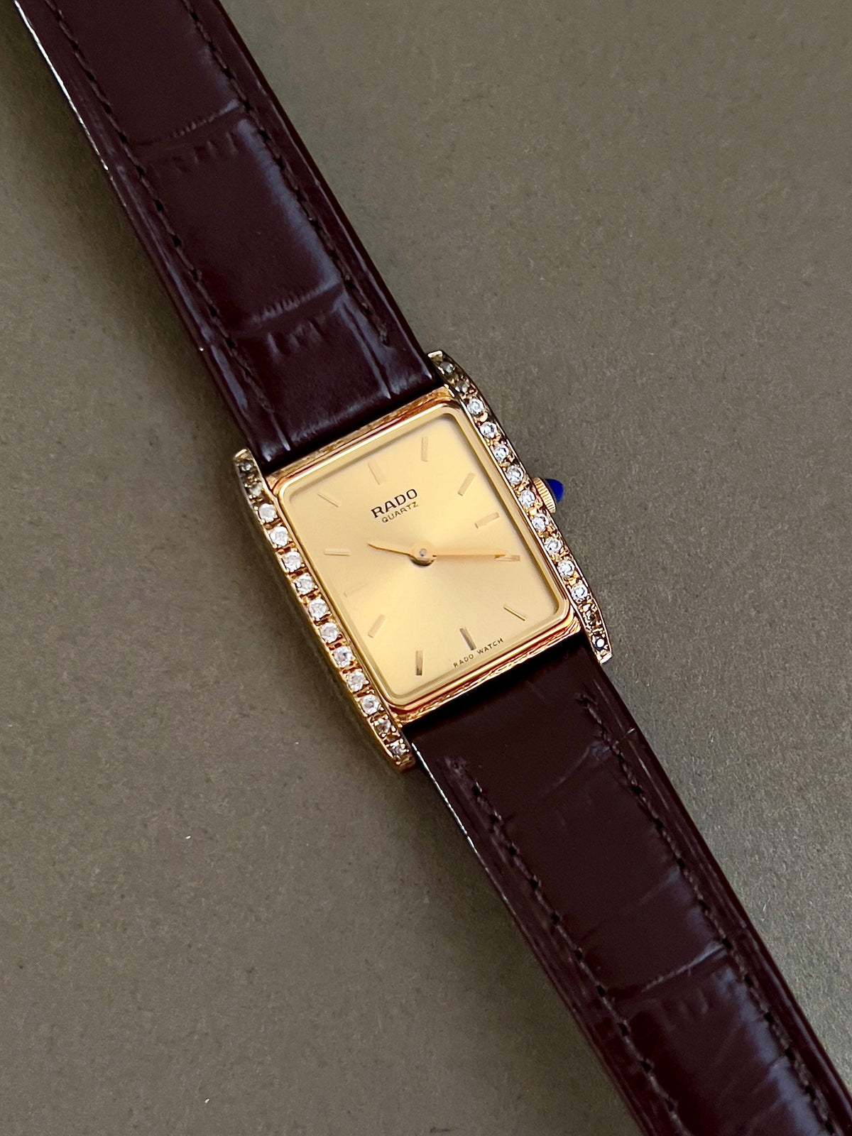 Vintage Rado tank women's watch with a champagne dial, diamond-set case and burgundy leather strap, shown from the front.