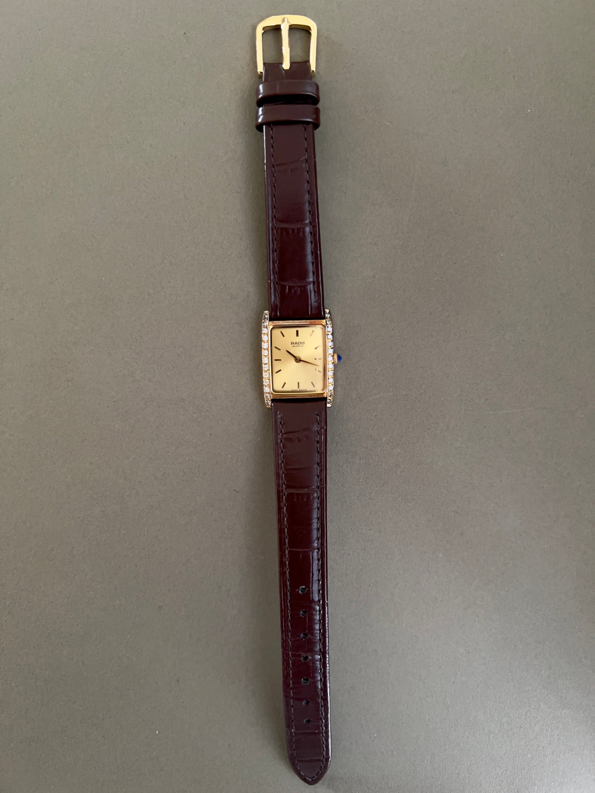 Vintage Rado tank women's watch with a champagne dial, diamond-set case and burgundy leather strap, shown full length.