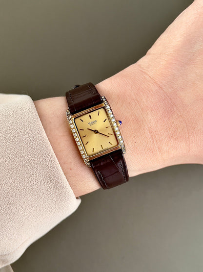 Vintage Rado tank women's watch with a champagne dial, diamond-set case and burgundy leather strap, worn on the wrist.