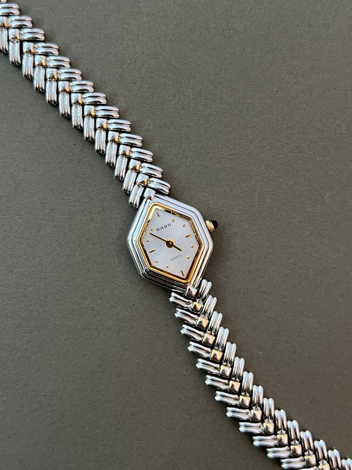 Vintage Rado two-tone sculpted women's watch with a pearl dial and herringbone bracelet, shown front-facing with the bracelet extended.