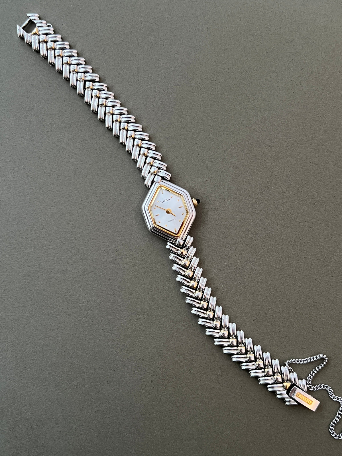 Vintage Rado two-tone sculpted women's watch with a pearl dial and herringbone bracelet, shown full length with the bracelet open.