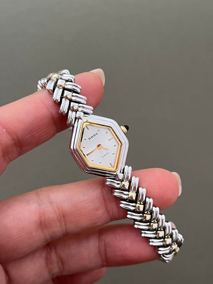 Vintage Rado two-tone sculpted women's watch with a pearl dial and herringbone bracelet, held in hand to show its petite proportions.