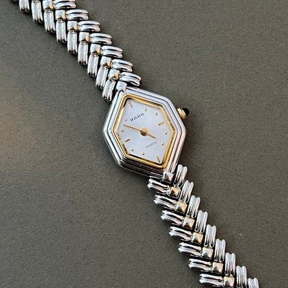 Vintage Rado two-tone sculpted women's watch with a pearl dial and herringbone bracelet, shown in a close front view.