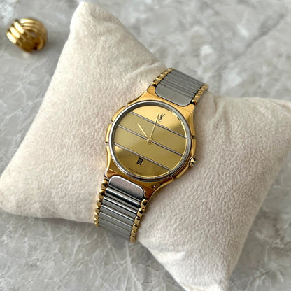 Vintage Yves Saint Laurent YSL Women’s watch with a striped gold dial, date window at six, gold tone case and integrated silver and gold tone bracelet, photographed on a cream velvet cushion.