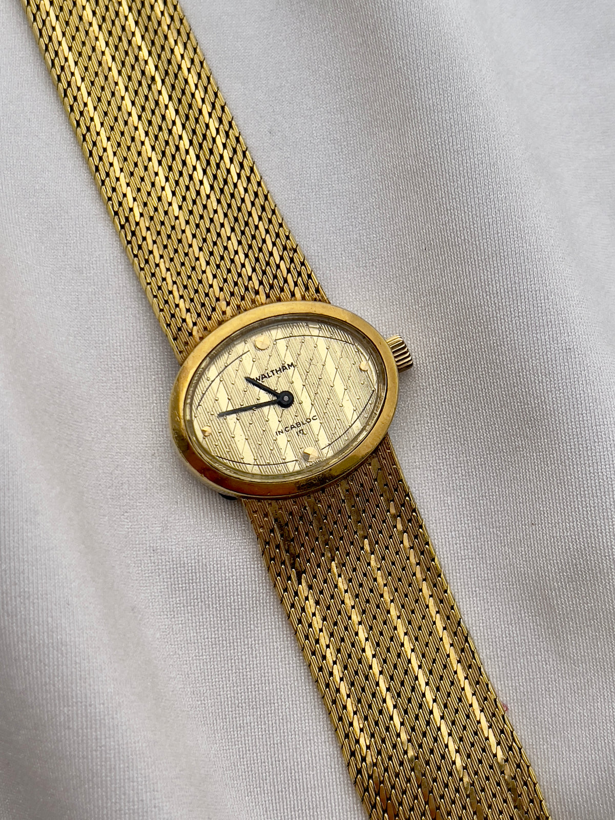 Waltham hand-wound watch featuring a round gold-tone case and textured champagne dial.