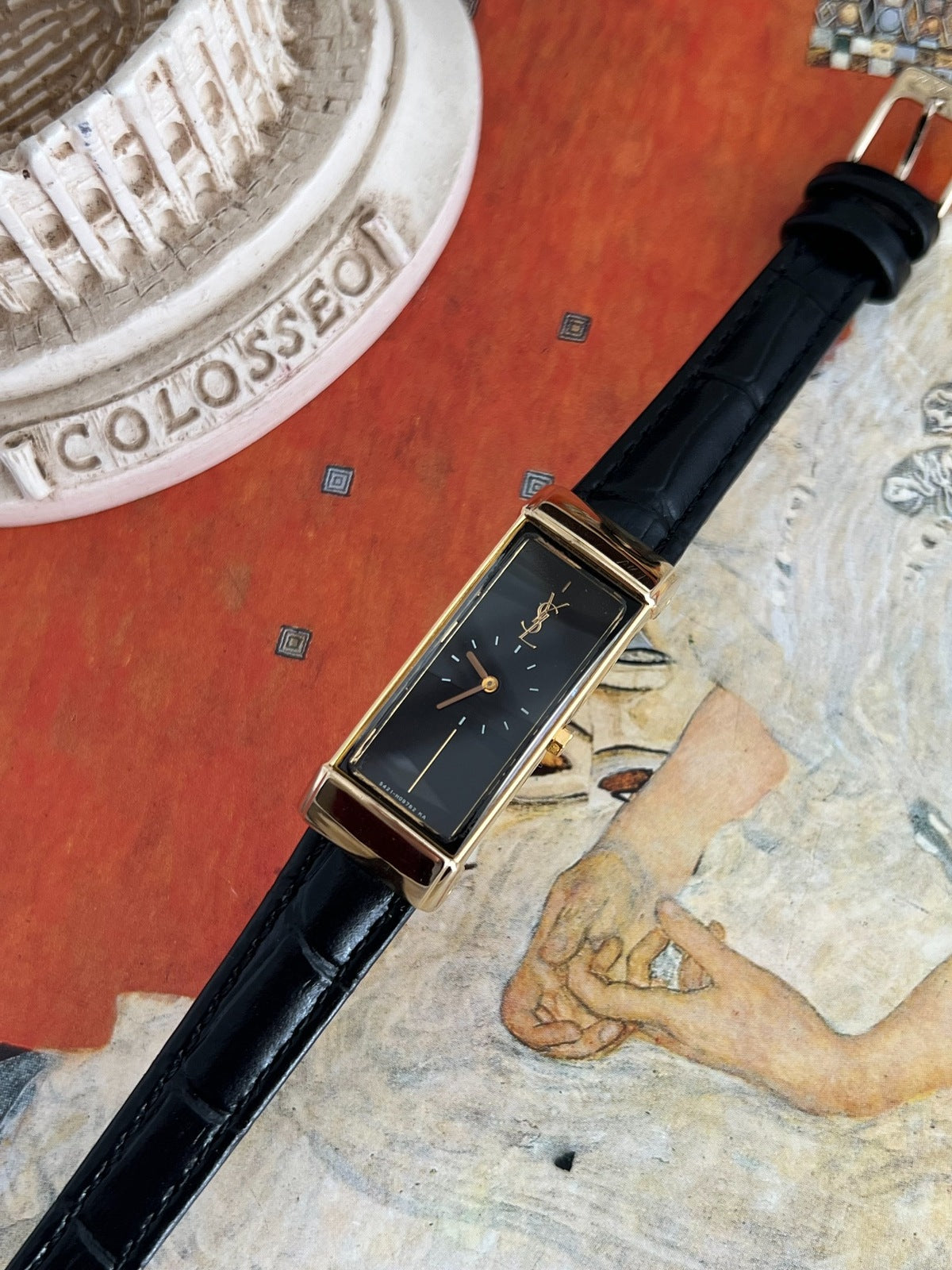 Close view of the Yves Saint Laurent black dial, gold monogram, two hands and polished rectangular gold tone frame.