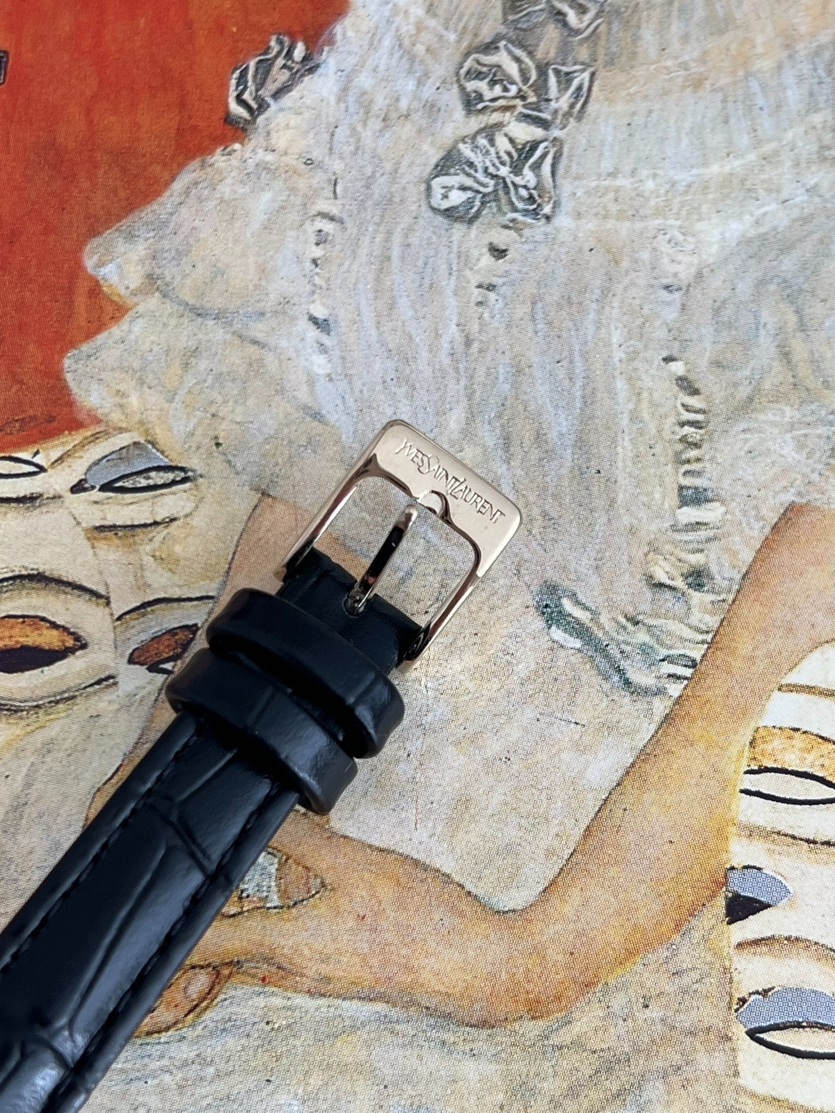 Close view of the pin buckle engraved Yves Saint Laurent on the black embossed leather strap.
