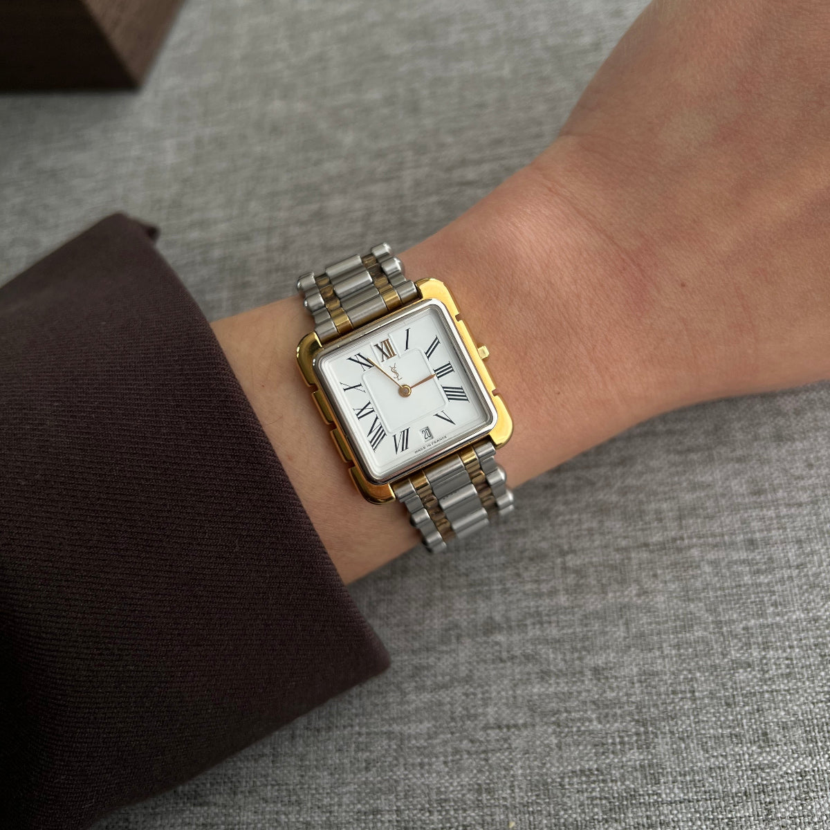 Yves Saint Laurent square luxury women’s watch with white Roman numeral dial and two tone bracelet worn on wrist
