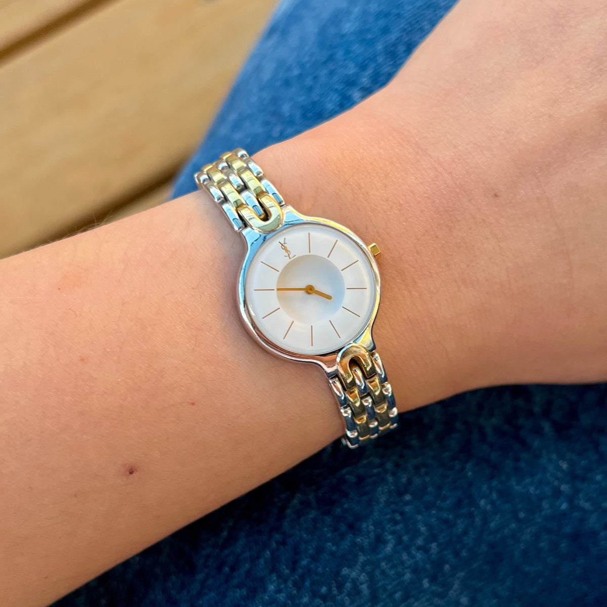 Yves Saint Laurent women’s watch with white medallion dial, domed crystal and two tone bracelet worn on wrist