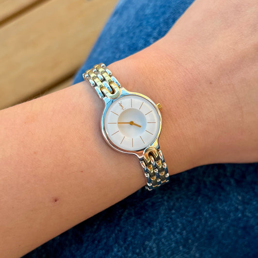 Yves Saint Laurent women’s watch with white medallion dial, domed crystal and two tone bracelet worn on wrist
